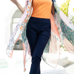 Woman wearing an orange top and navy pants with a floral shawl outdoors.