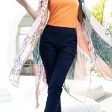 Woman wearing an orange top and navy pants with a floral shawl outdoors.