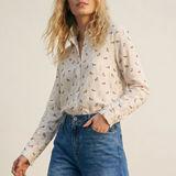 Woman wearing a patterned shirt and blue jeans against a plain background