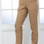 Person wearing beige pants and black boots in front of a white paneled wall.