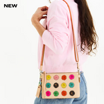 Person wearing a pink sweater with a beige crossbody bag featuring colorful floral patterns on a white background.