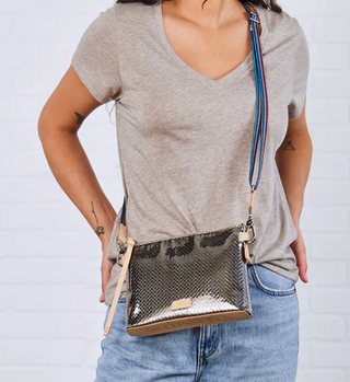 Person wearing a gray t-shirt and blue jeans with a snakeskin crossbody bag on a light gray background