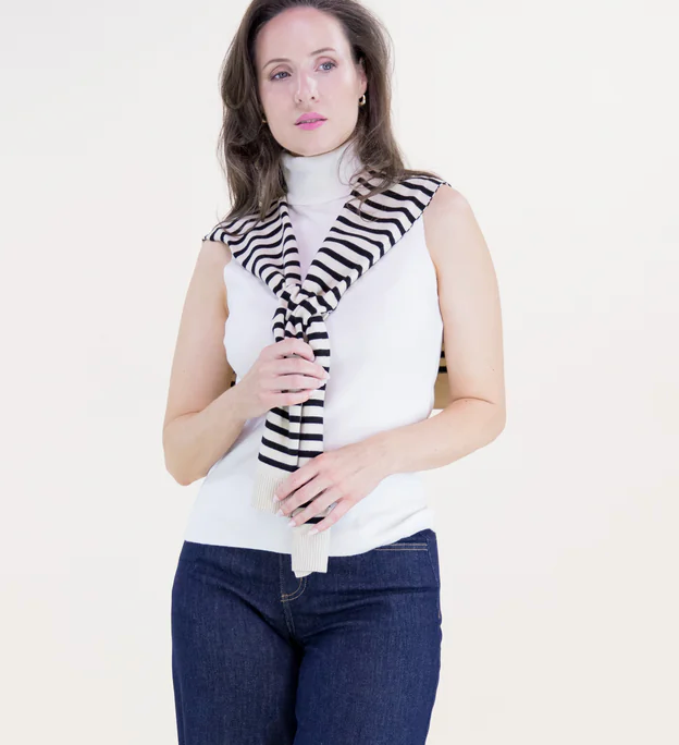 Woman wearing a white turtleneck and blue jeans with a black and white striped scarf on a white background
