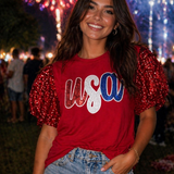 Woman wearing a red 'USA' shirt with sequin sleeves in front of fireworks