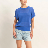 Person wearing a blue sweater and denim shorts on a plain background