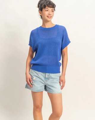 Person wearing a blue sweater and denim shorts on a plain background
