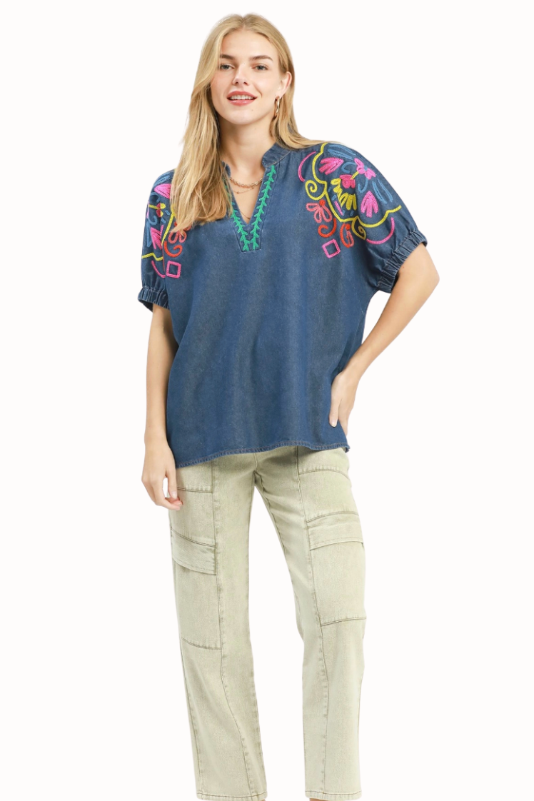Woman wearing a blue embroidered top and beige pants on a white background