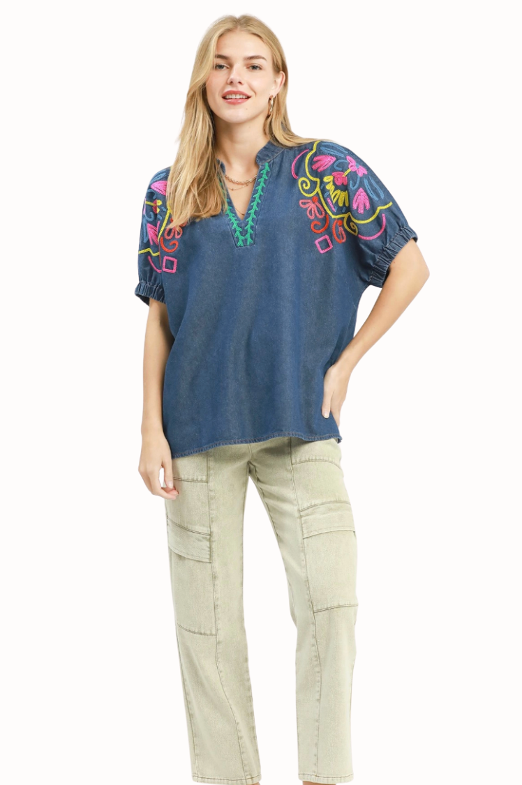 Woman wearing a blue embroidered top and beige pants on a white background