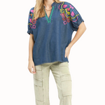 Woman wearing a blue embroidered top and beige pants on a white background