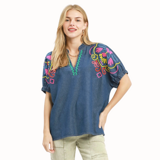 Woman wearing a blue embroidered top and beige pants on a white background