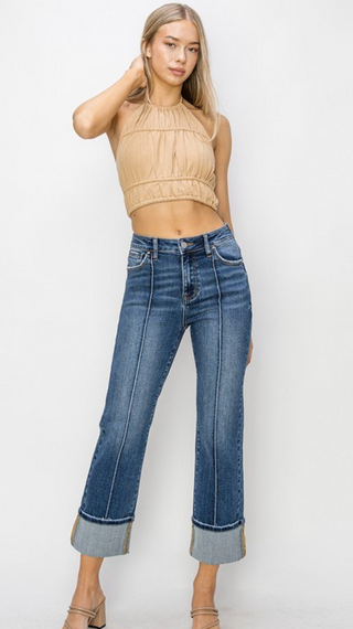 Woman wearing a beige crop top and blue jeans on a white background