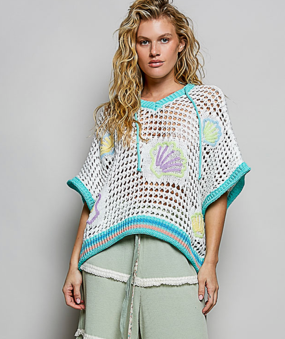 Woman wearing a crochet poncho with shell patterns on a plain background