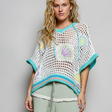 Woman wearing a crochet poncho with shell patterns on a plain background