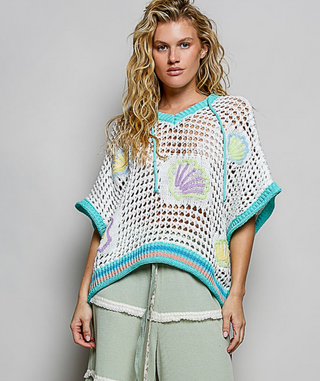 Woman wearing a crochet poncho with shell patterns on a plain background