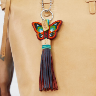 Butterfly keychain with tassel attached to a beige bag