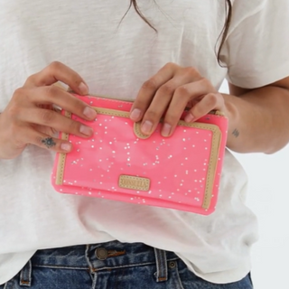 Person holding a pink wallet with white polka dots and gold accents.