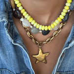 Necklace with yellow beads, gold chain, and star pendant worn over a denim jacket.
