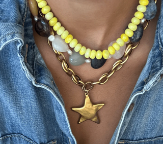 Necklace with yellow beads, gold chain, and star pendant worn over a denim jacket.