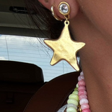 Gold star-shaped earring worn by a person with a blurred background
