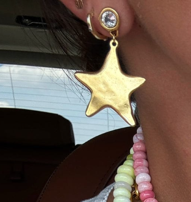 Gold star-shaped earring worn by a person with a blurred background