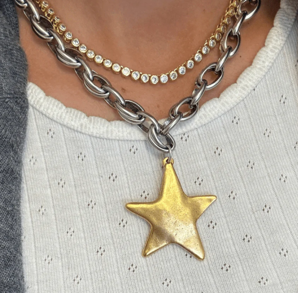 Necklace with a gold star pendant worn by a person on a light-colored garment.
