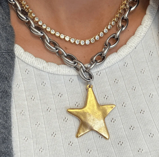 Necklace with a gold star pendant worn by a person on a light-colored garment.