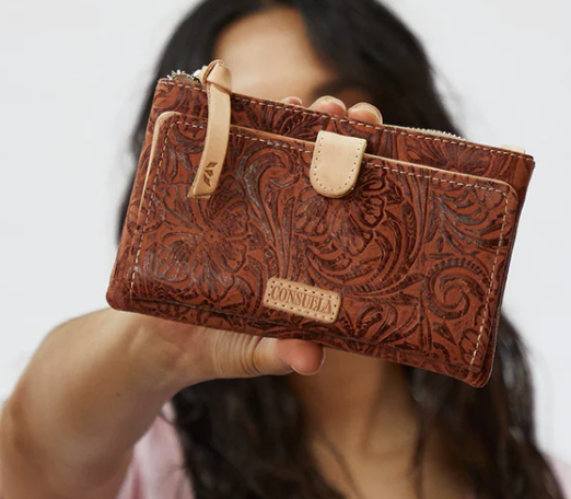 Person holding a brown leather wallet with intricate patterns and 'Sonsuela' branding.
