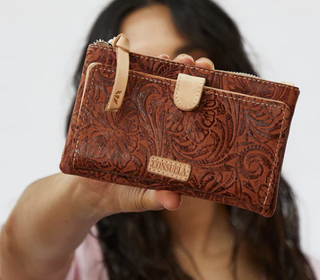 Person holding a brown leather wallet with intricate patterns and 'Sonsuela' branding.