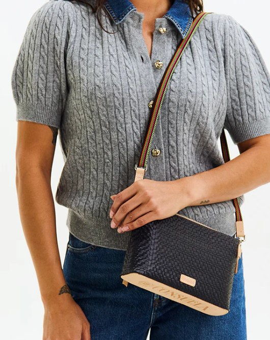 Person wearing a gray cable knit sweater holding a black handbag with a strap.