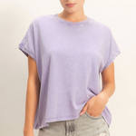 Woman wearing a light purple oversized t-shirt and denim shorts on a plain background
