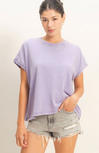 Woman wearing a light purple oversized t-shirt and denim shorts on a plain background