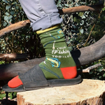 Person wearing colorful socks with fishing-themed design on a wooden log outdoors.
