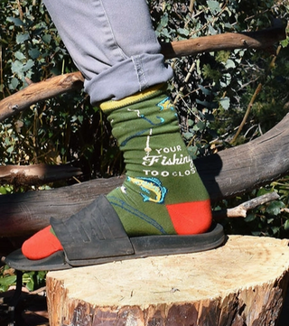 Person wearing colorful socks with fishing-themed design on a wooden log outdoors.
