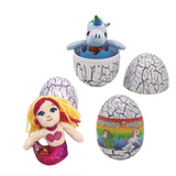A toy set featuring a mermaid plush with yellow and pink hair and a glittery purple tail, a blue unicorn plush sitting inside a cracked white egg, and two cracked white eggs with colorful printed graphics on a plain white background.