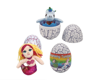 A toy set featuring a mermaid plush with yellow and pink hair and a glittery purple tail, a blue unicorn plush sitting inside a cracked white egg, and two cracked white eggs with colorful printed graphics on a plain white background.