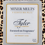 A square plastic clamshell package of Tyler Candle Company 'Focused on Fragrance' scented wax melts. The white label features black and gold typography, set against a leopard print background.