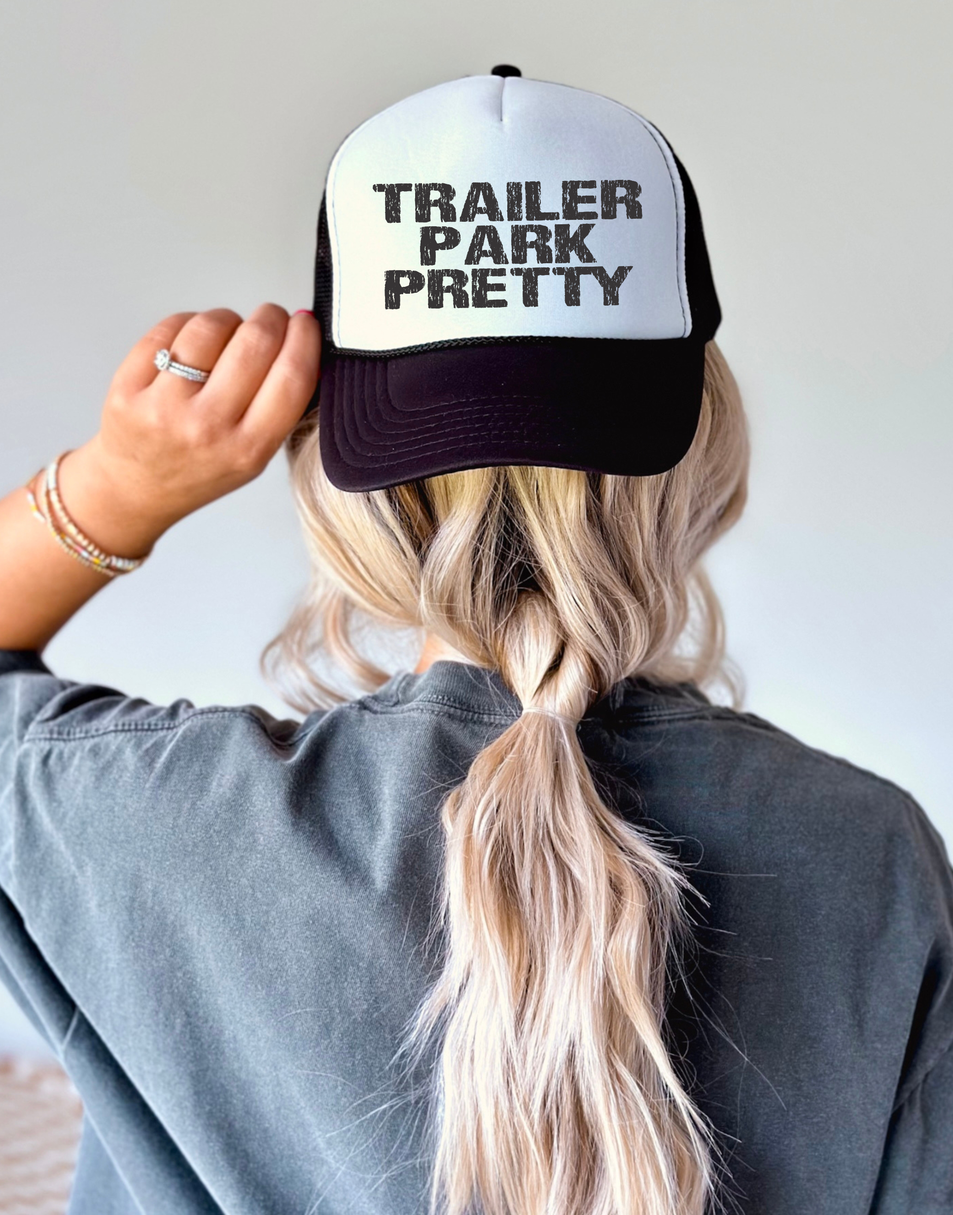 Person wearing a cap with 'Trailer Park Pretty' text on a plain background