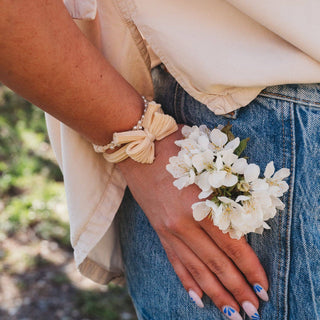 Person wearing a beige shirt and blue jeans with a white flower on their lap, holding a small bouquet of white flowers.