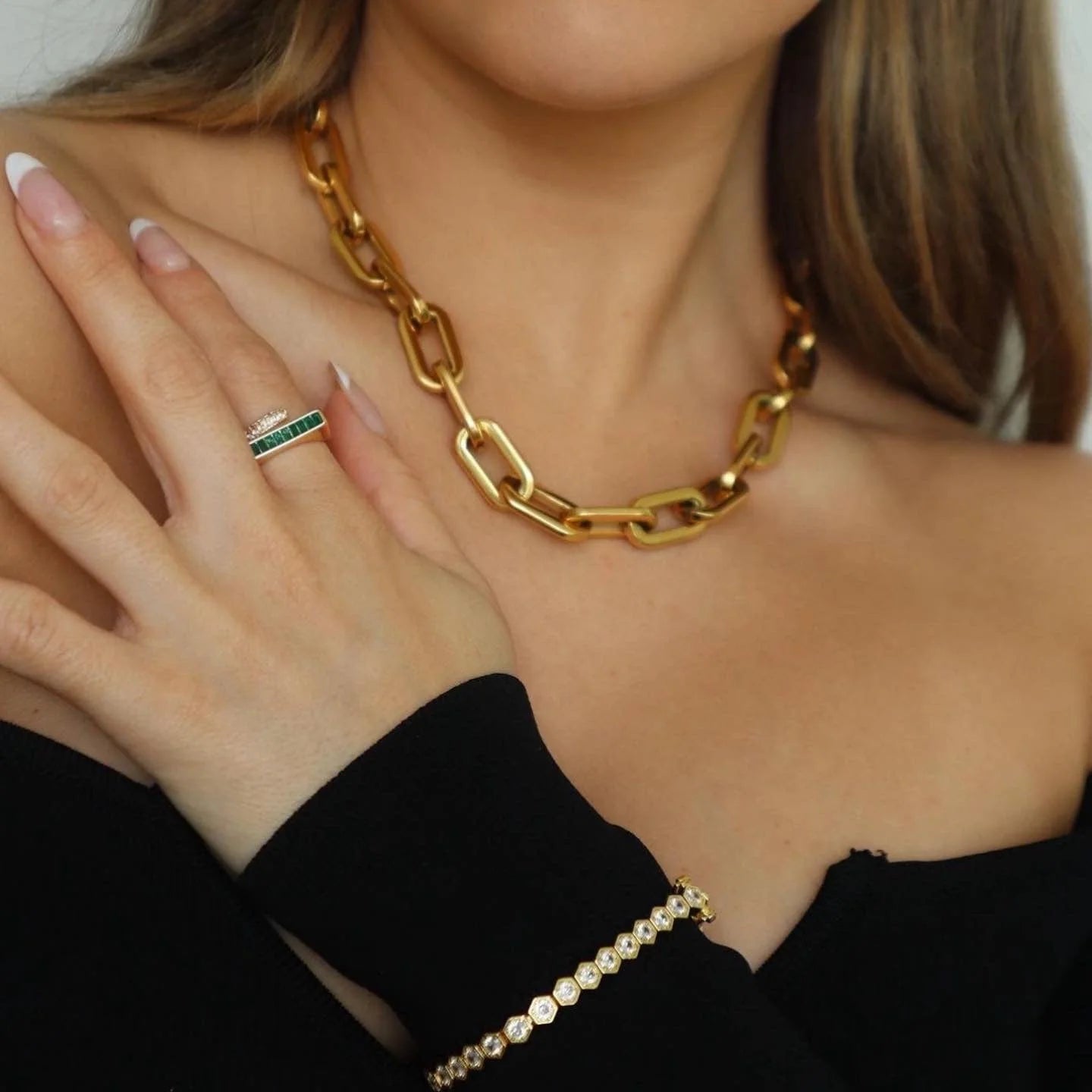 Gold chain necklace, ring, and bracelet on a person wearing a black top.