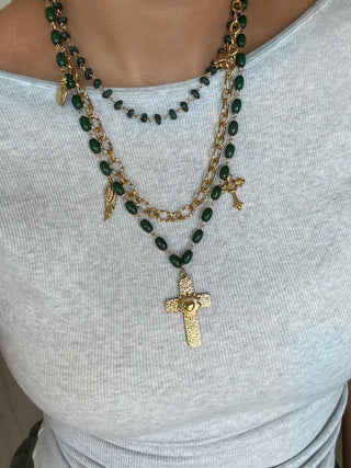 Green beaded necklace with gold cross pendant on a white top