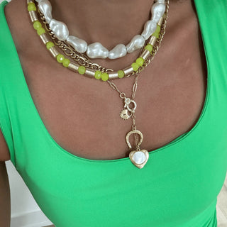 Charm necklace stached witho ther necklaces, female in green tank.