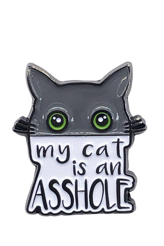 Enamel pin with a black frame shaped like a cat's head with green eyes, and a humorous text caption 'my cat is an asshole'.
