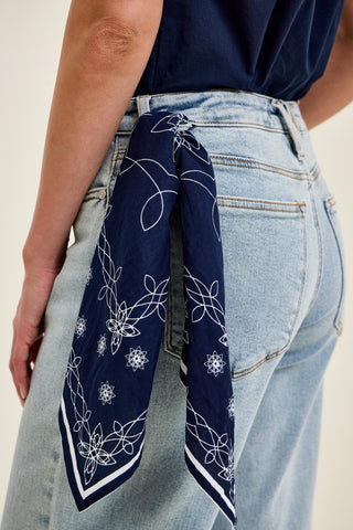 Navy blue bandana with white patterns tied around a person's waist, wearing light blue jeans.