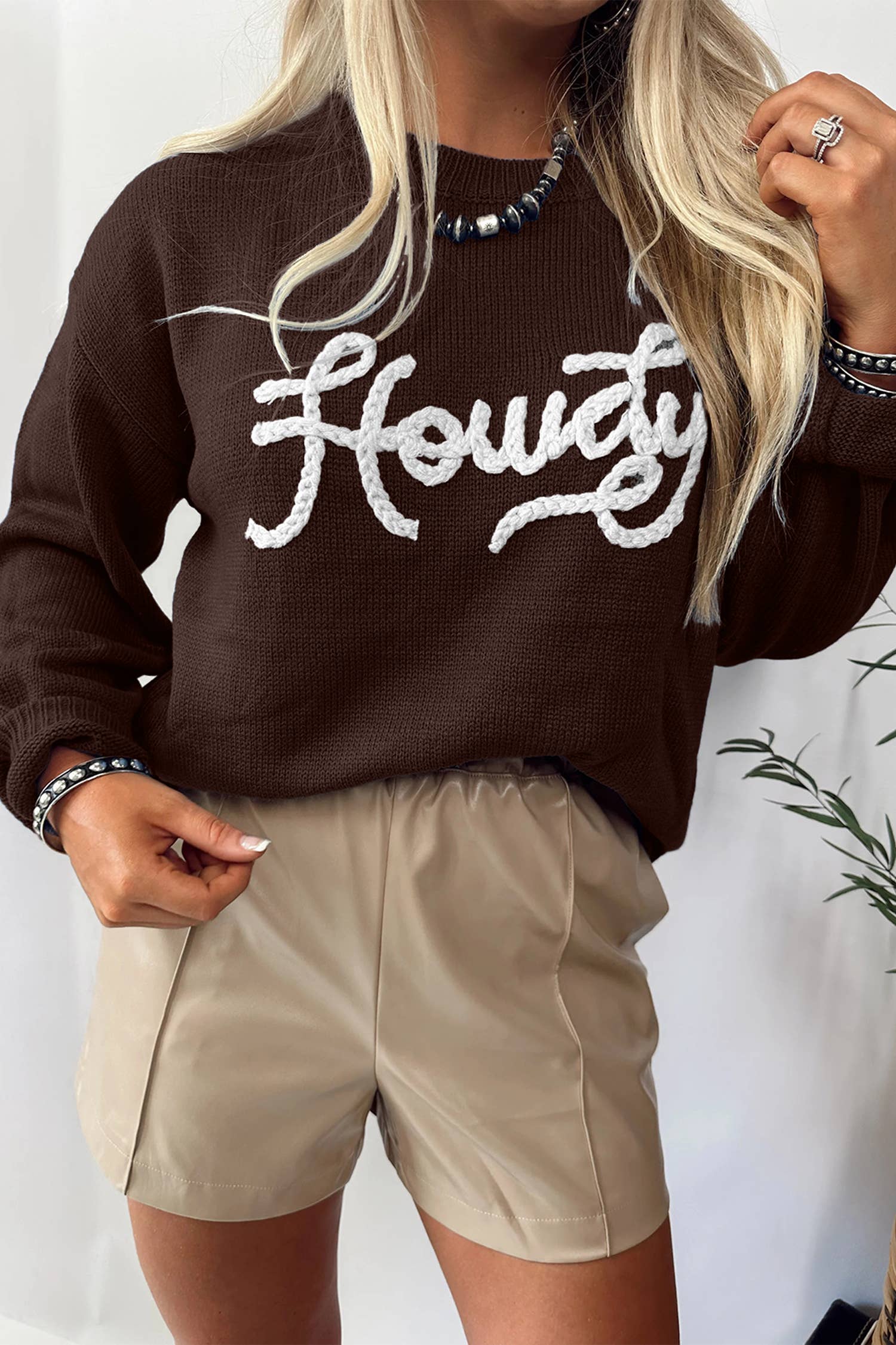 Person wearing a brown sweater with 'Howdy' text and beige shorts against a white background