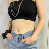 Person wearing a black strapless top and blue jeans with a neutral background