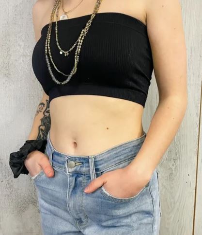 Person wearing a black strapless top and blue jeans with a neutral background