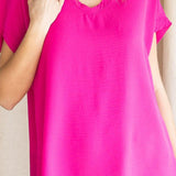 A model wearing a short-sleeved hot pink top with a round neckline and raw edge hems.