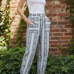 Model wearing cactus stripe jogger pants with white tank top in front of brick wall with greenery