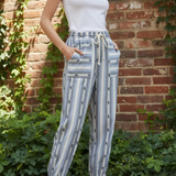 Model wearing cactus stripe jogger pants with white tank top in front of brick wall with greenery