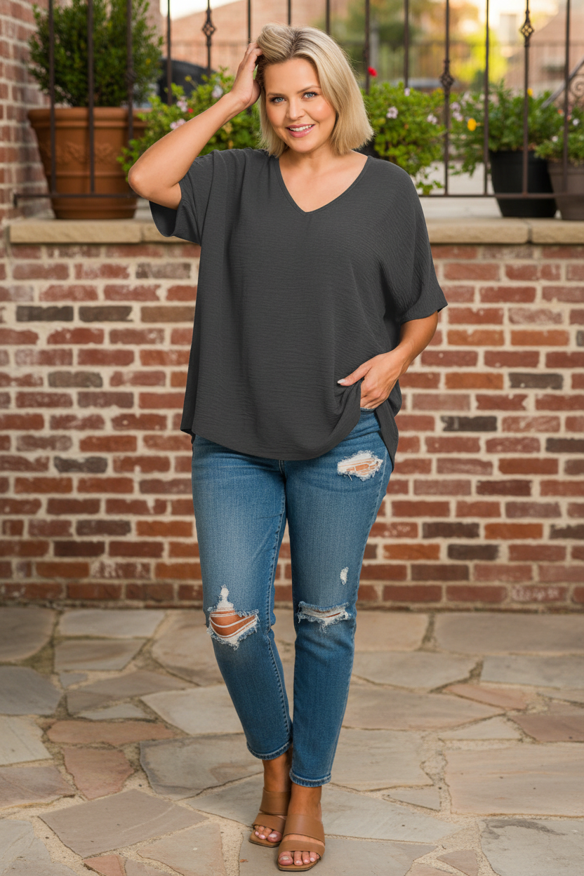 Woman wearing charcoal gray v-neck top standing in front of brick wall terrace